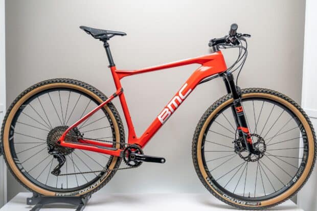 A red BMC mountain bike stands against a neutral wall with tan tires and disc brakes, 2K Desktop Wallpaper