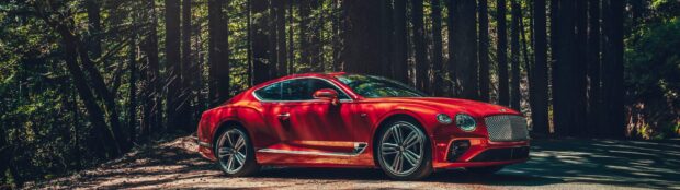 A red Bentley Continental GT parked on a forest road with sunlight filtering through trees, 4K Desktop Wallpaper