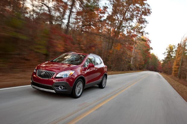 A red Buick Encore drives through a forest road with fall colors visible, 2K Desktop Wallpaper
