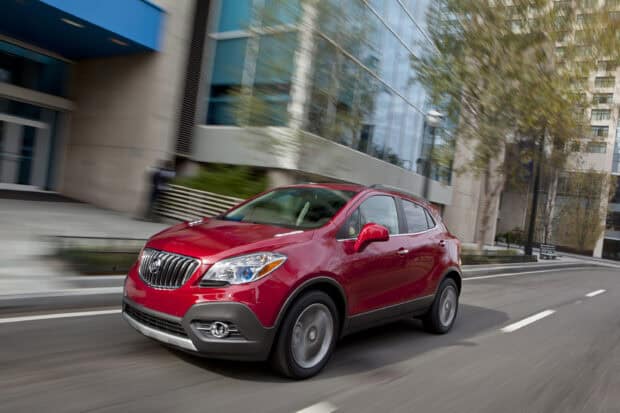 A red Buick Encore drives smoothly through an urban area with buildings in the background, 2K Desktop Wallpaper