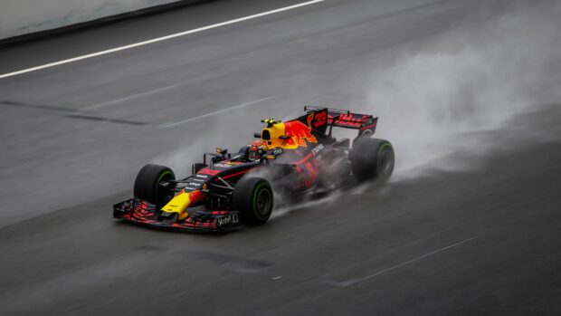 A Red Bull race car is speeding on a wet race track with tire smoke visible, 4K Desktop Wallpaper