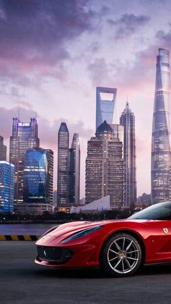 A red Ferrari 812 Gts is parked with a city skyline in the background during dusk, 4K Mobile Wallpaper