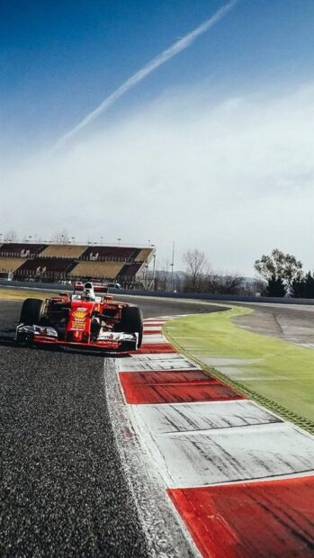 A red Formula One car races on a curving section of the race track under a blue sky, HD Mobile Wallpaper