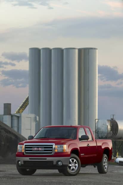 A red GMC Sierra is parked in front of large industrial silos during twilight, 2K Desktop Wallpaper