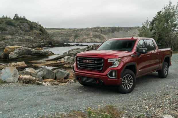 A red GMC Sierra truck is parked beside rocks and water under a cloudy sky, HD Desktop Wallpaper