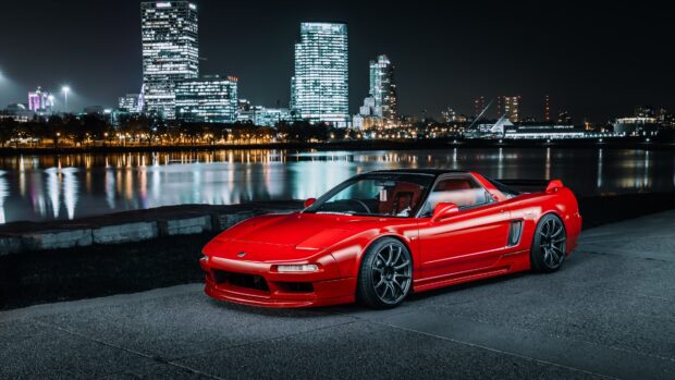 A red Honda NSX is parked on a riverside road with city lights reflecting on the water behind it, 4K Desktop Wallpaper