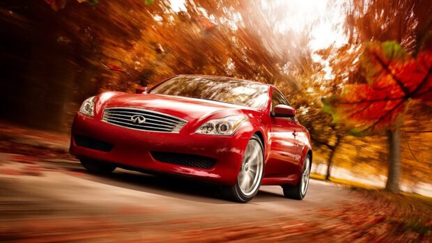 A red Infiniti G37 drives fast on a road surrounded by autumn trees and falling leaves, 4K Desktop Wallpaper