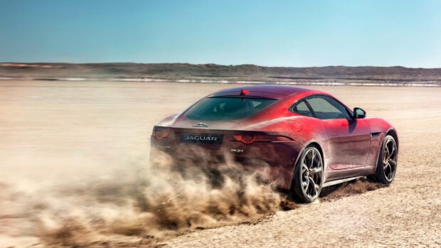 A red Jaguar F Type is kicking up dust as it speeds across a vast desert landscape, 2K Desktop Wallpaper