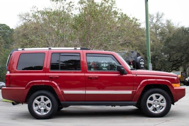 A red Jeep Commander is parked beside trees and other vehicles in a calm outdoor setting, HD Desktop Wallpaper