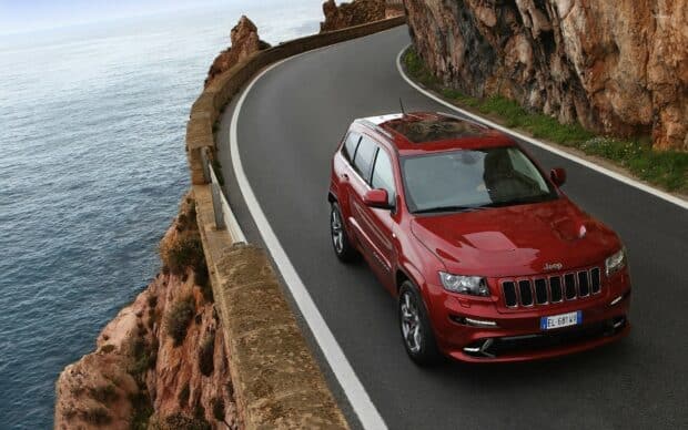 A red Jeep Grand Cherokee is driving along a winding coastal road beside cliffs and the ocean, HD Desktop Wallpaper