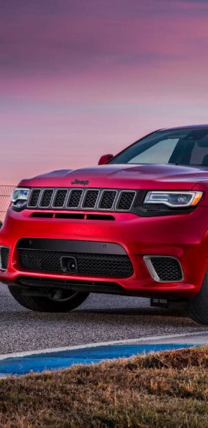 A red Jeep Grand Cherokee is parked on a road with a purple sky at sunset, 2K Mobile Wallpaper