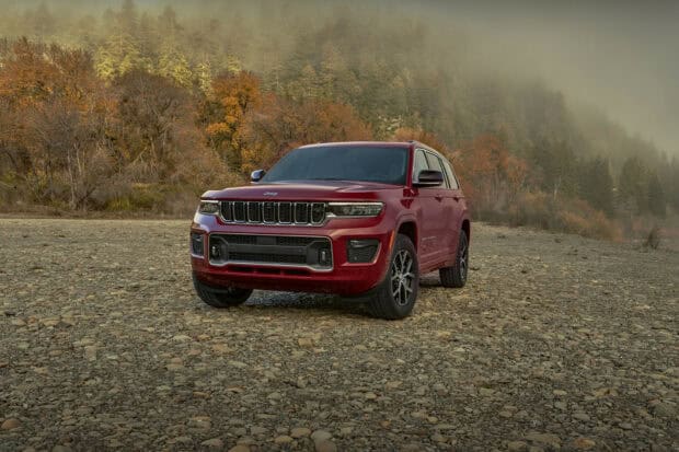 A red Jeep Grand Cherokee is parked on a rocky riverbed with autumn trees and misty hills in the background, HD Desktop Wallpaper