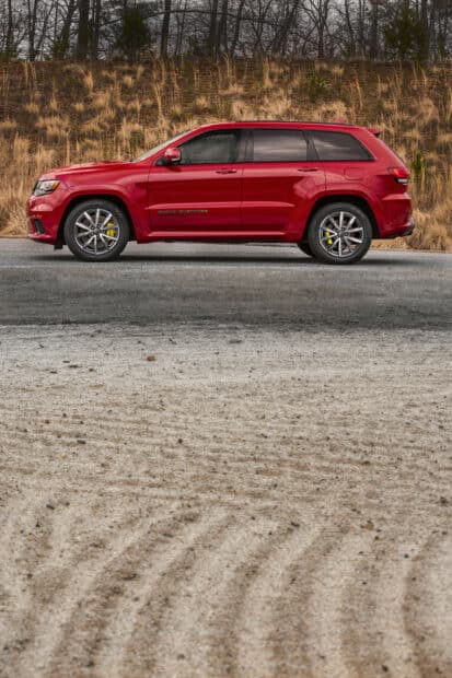 A red Jeep Grand Cherokee is parked by a grassy hillside with dry vegetation, 2K Mobile Wallpaper