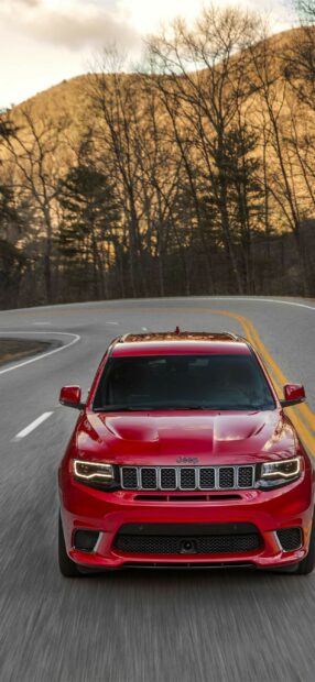 A red Jeep Grand Cherokee drives on a winding road surrounded by bare trees, 2K Phone Wallpaper