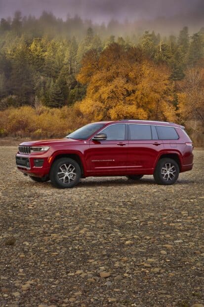 A red Jeep Grand Cherokee is parked on a rocky ground with autumn trees and forest in the background, 2K Mobile Wallpaper