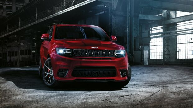 A red Jeep Grand Cherokee is parked inside a dimly lit industrial building with its headlights on, 4K Desktop Wallpaper