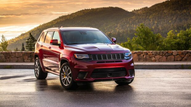A red Jeep Grand Cherokee is parked on a wet road with forested mountains in the background during sunset, 2K Desktop Wallpaper