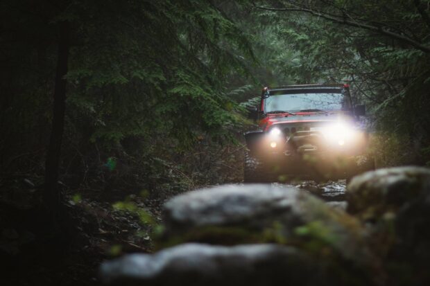 A red Jeep is driving off road through a dense forest path with its headlights on, HD Desktop Wallpaper