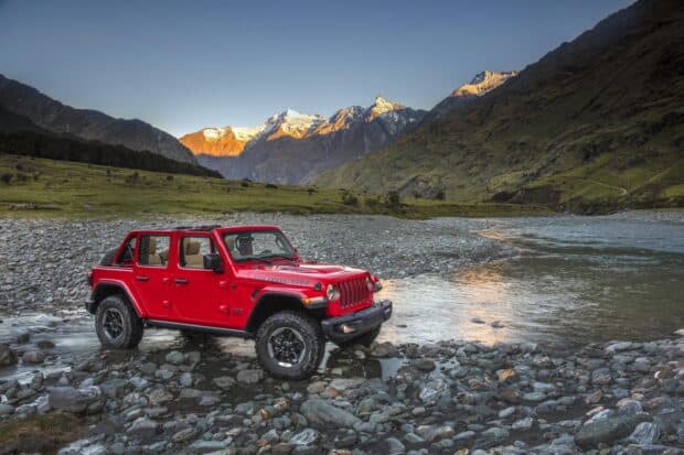 A red Jeep is driving off road near a rocky river with mountains in the background, 2K Desktop Wallpaper