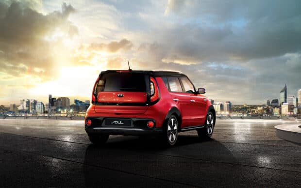 A red Kia Soul is parked with a city skyline view during sunset under a cloudy sky, HD Desktop Wallpaper