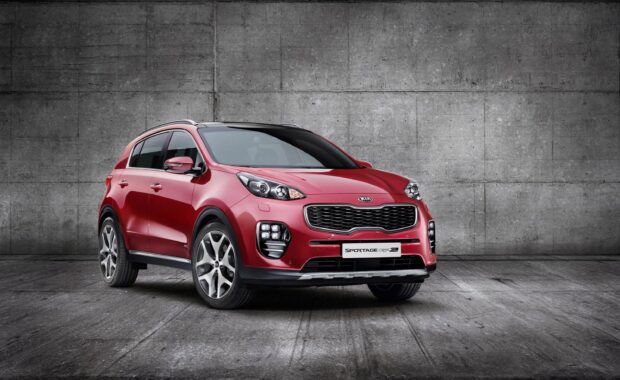 A red Kia Sportage is parked indoors against a large concrete wall showcasing its sleek design, 2K Desktop Wallpaper