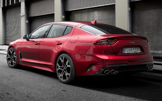A red Kia Stinger sports car is parked near industrial doors showing its sleek design, HD Desktop Wallpaper