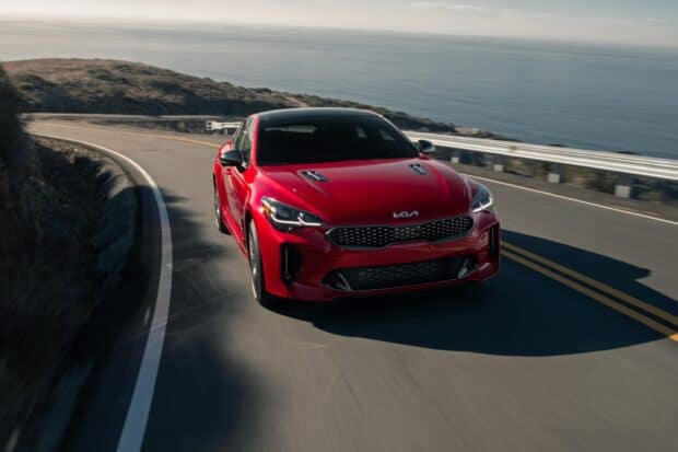 A red Kia Stinger driving smoothly along a winding coastal road with the ocean in the background, HD Desktop Wallpaper