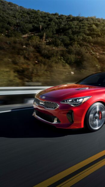 A red Kia Stinger is driving fast on a winding mountain road, 4K Phone Wallpaper