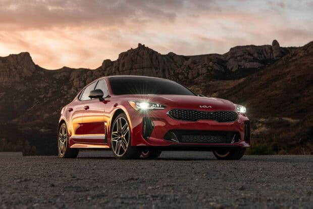 A red Kia Stinger is parked on a gravel road with mountains in the background at sunset, HD Desktop Wallpaper