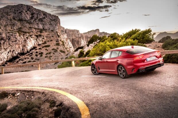 A red Kia Stinger is parked on a winding mountain road with rocky cliffs in the background, HD Desktop Wallpaper