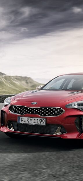 A red Kia Stinger is driving on a winding mountain road under a cloudy sky, HD Phone Wallpaper