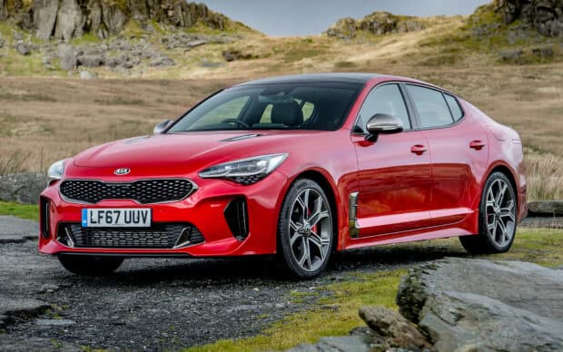 A red Kia Stinger is parked on a rugged countryside road with hills in the background, HD Desktop Wallpaper
