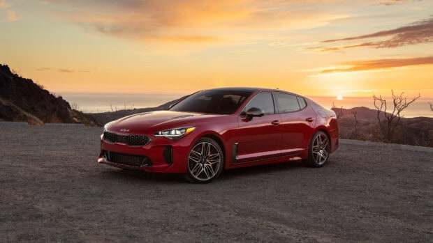 A red Kia car is parked on a mountain road during sunset, with the sun low on the horizon, 4K Desktop Wallpaper