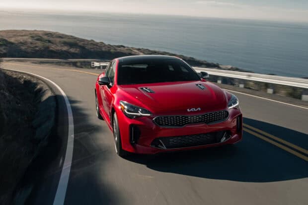 A red Kia car is driving along a winding coastal road next to the ocean, HD Desktop Wallpaper