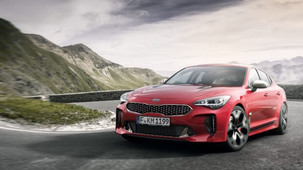 A red Kia car is driving on a curvy mountain road with scenic hills in the background, 4K Desktop Wallpaper