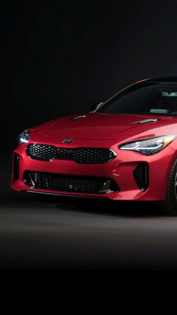 A red Kia car shows a sleek front grille and illuminated headlights, 2K Phone Wallpaper