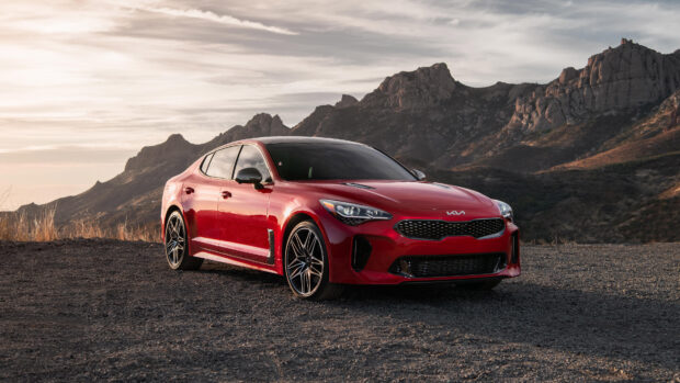 A red Kia car is parked on a dirt road with rugged mountains in the background under a cloudy sky, 4K Desktop Wallpaper