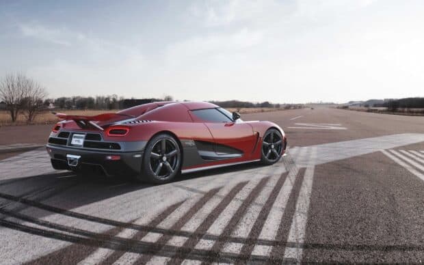 A red Koenigsegg is parked on a runway with clear skies and trees in the background, 2K Desktop Wallpaper