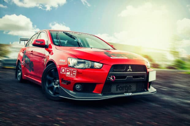 A red Lancer Evo car is shown drifting on a racetrack under a bright sky, HD Desktop Wallpaper