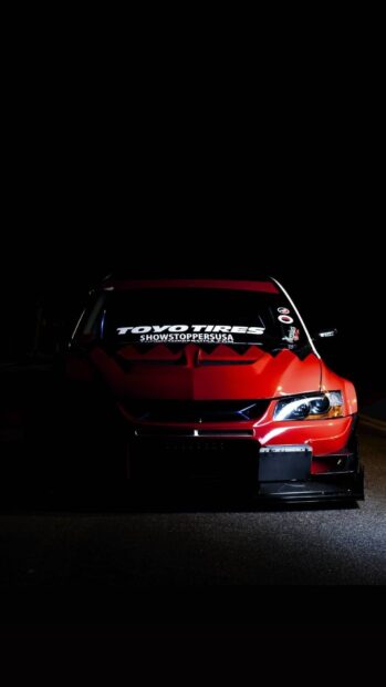 A red Lancer Evo features bright headlights and custom decals in a dark setting, HD Phone Wallpaper
