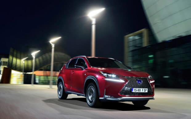 A red Lexus NX drives through a modern city street under streetlights at night, 2K Desktop Wallpaper