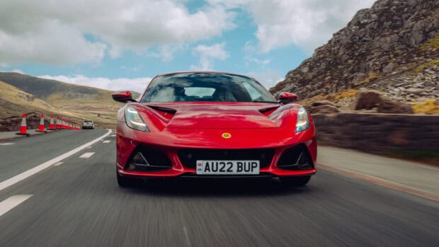 A red Lotus Emira drives on a winding mountain road under a cloudy sky, 2K Desktop Wallpaper