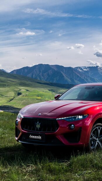 A red Maserati Levante is parked on grass with mountains and a blue sky in the background, 4K Phone Wallpaper
