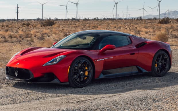 A red Maserati MC20 is parked on a dirt road surrounded by desert landscape and wind turbines, HD Desktop Wallpaper