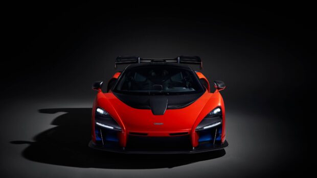 A red McLaren Senna is shown from the front with illuminated headlights in a dark studio setting, 4K Desktop Wallpaper