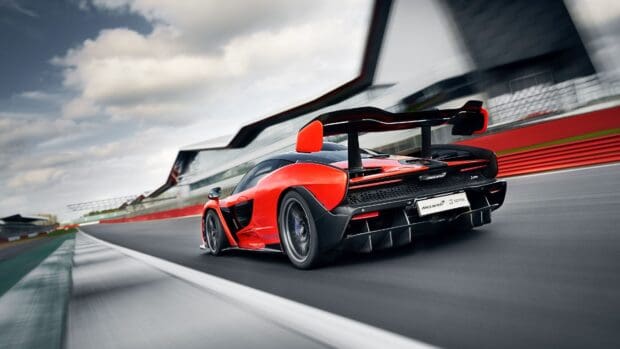 A red McLaren Senna is seen racing on a track under cloudy skies with motion blur in the background, 4K Desktop Wallpaper