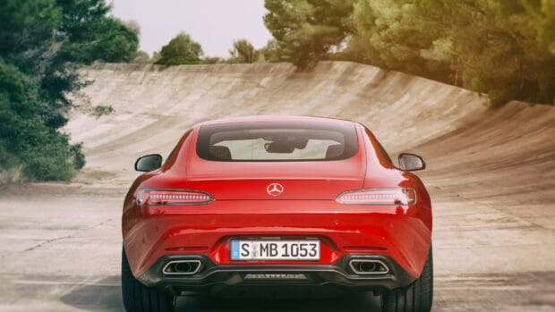 A red Mercedes Benz AMG GT is parked on a curved concrete road surrounded by trees, 4K Desktop Wallpaper