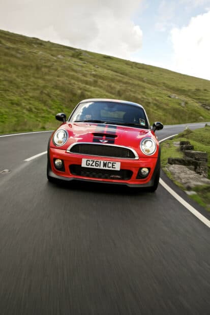 A red Mini Cooper is driving along a curved mountain road surrounded by green hills, HD Mobile Wallpaper