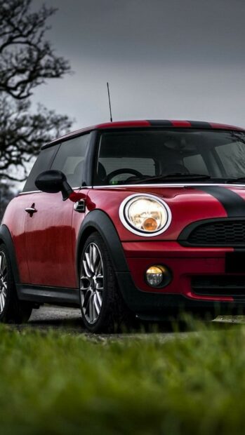 A red Mini Cooper with black racing stripes is parked outdoors under a cloudy sky, HD Mobile Wallpaper