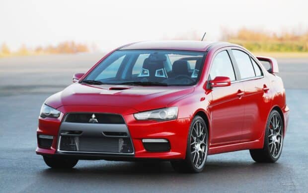 The red Mitsubishi Lancer Evo is parked on a clear road under soft daylight, HD Desktop Wallpaper